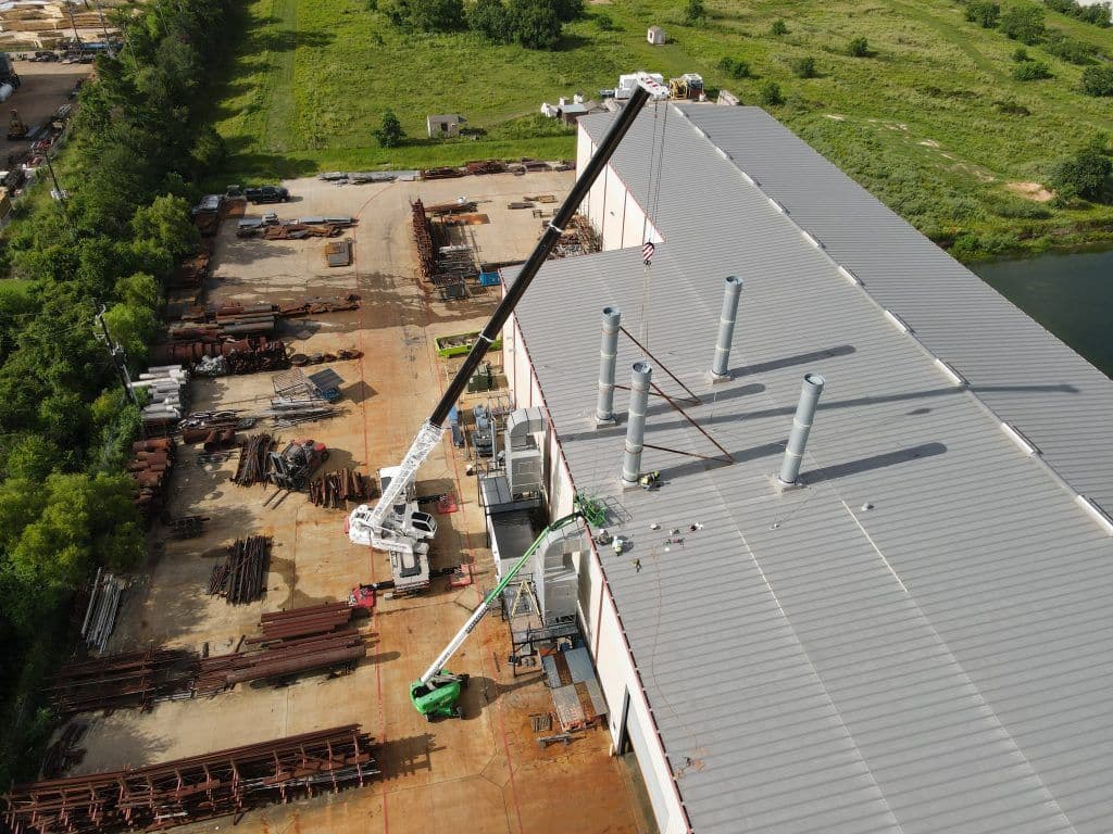 Aerial view of industrial building with crane and exhaust stacks in a storage yard.
